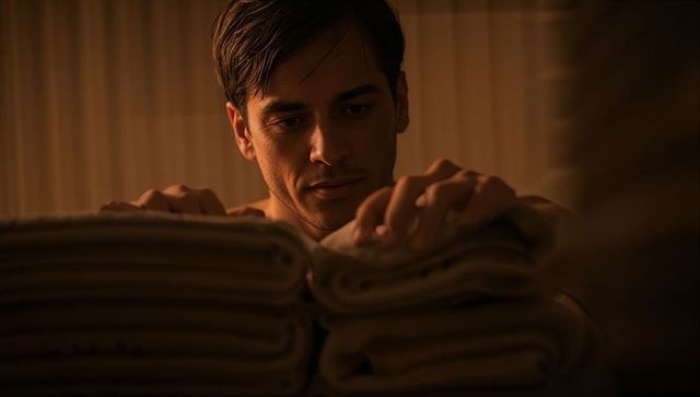 Young man inspecting folded towels in linen closet warm moody hospitality portrait