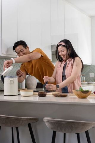 Asian couple cooking at kitchen island, man opening rice cooker, woman using mortar and pestle
