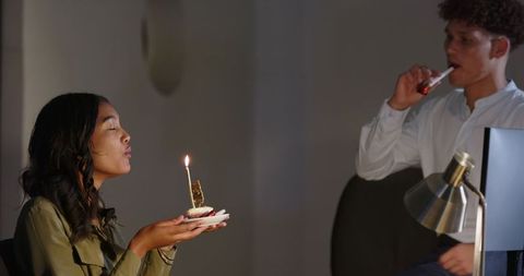 Colleagues celebrating birthday with cupcake and candle at office desk