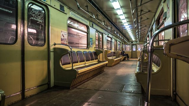 Spacious retro subway interior featuring rows of muted yellow metal seats. Dim fluorescent lighting highlights worn-out but functional design. Ideal for concepts involving public transportation, urban life, nostalgia, and solitude in metropolitan settings.