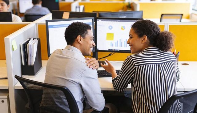 Colleagues collaborating at dual-monitor workstation analyzing business charts