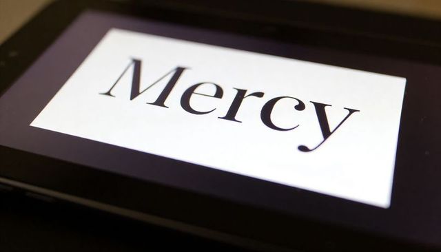 Tablet displaying mercy word glowing on dark desk minimal moody concept