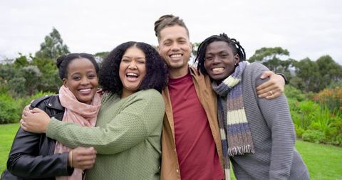 Laughing diverse friends hugging in park on overcast day