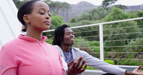 African american couple practicing outdoor meditation on balcony with green mountain view