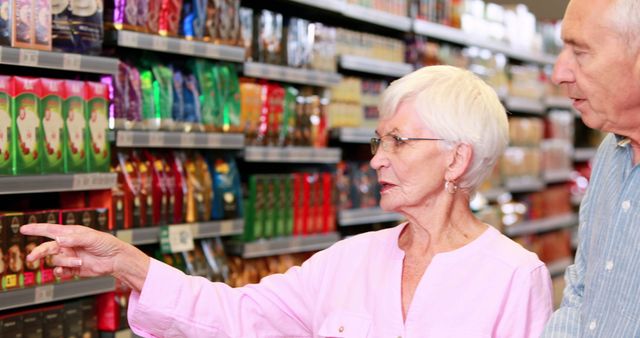 Senior couple browsing food products in supermarket aisle. Ideal for concepts related to senior lifestyle, grocery shopping, consumer habits, and retail environments. Can be used in marketing materials for supermarkets, grocery delivery services, and age-defying products.