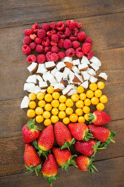 Colorful assortment of fresh fruits including strawberries, raspberries, coconut pieces, and golden berries arranged on a wooden board. Ideal for use in healthy eating promotions, diet and nutrition articles, summer recipes, and organic food advertisements.