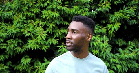 Contemplative african man in light t-shirt standing in lush green garden