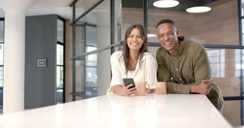 Colleagues Smiling in Modern Office Holding Smartphone and Coffee