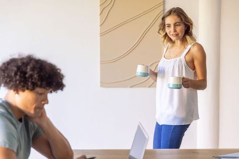 Serving morning coffee while partner working on laptop in bright minimal home interior