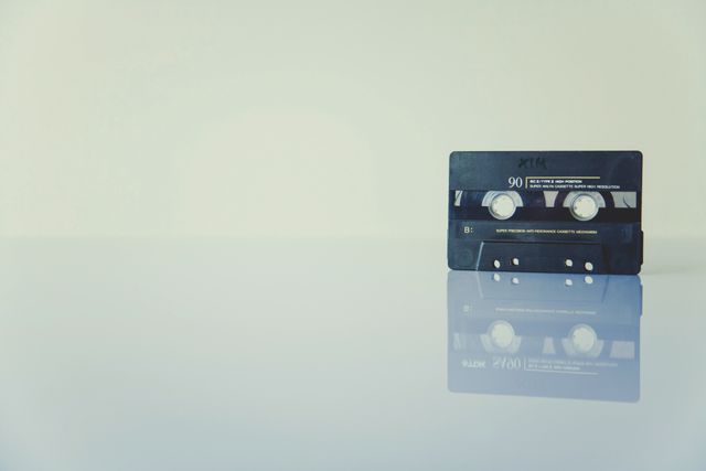 Old audio cassette tape resting on reflective surface, evoking nostalgia for 1980s music and analog recording. Suitable for articles on retro technology, music history, collectibles, or vintage media. Ideal for designs that require a touch of nostalgia and retro appeal.