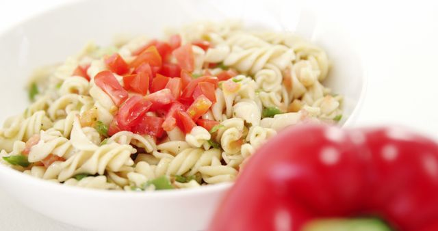 This image depicts a delicious pasta salad in a white bowl garnished with diced red bell peppers and herbs. Perfect for illustrating healthy eating, vegetarian recipes, summer meals, and homemade goodness. Ideal for food blogs, cookbooks, or nutrition websites.