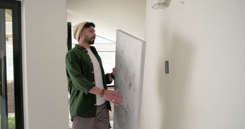 Indian man carrying large textured canvas through modern home hallway while moving artwork