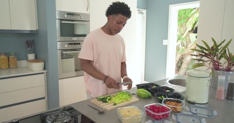 Young man preparing healthy meal prep bowls on modern kitchen island with fresh vegetables