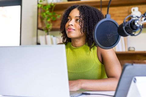 African woman recording podcast from home office with laptop and condenser microphone