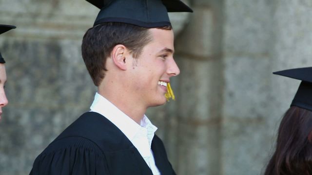 Young male student smiling in cap and gown during graduation ceremony. Perfect for depicting academic milestones, educational content, university promotions, and success stories.