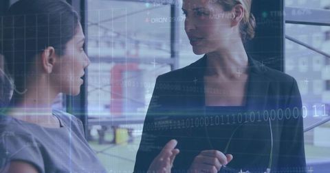 Businesswomen discussing data overlay while collaborating in modern glass office meeting