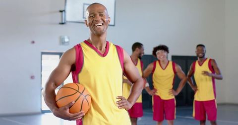 Smiling black team captain holding basketball with diverse male teammates on indoor court