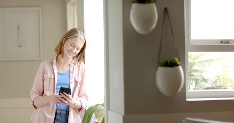 Woman enjoying smartphone in bright modern home interior with hanging plants