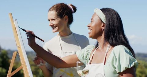 Friends Painting Outdoors Against Scenic Hills Holding Wine Glasses