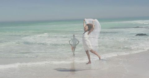 Joyful woman leaping with sheer veil on turquoise ocean shoreline, dreamy double exposure