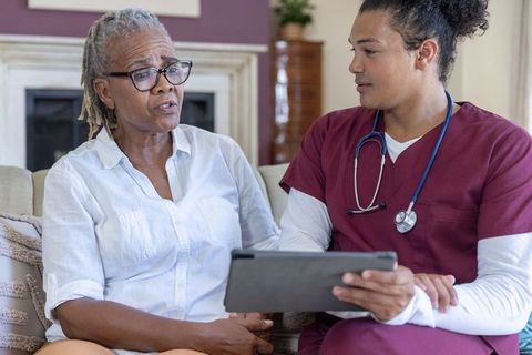 Senior african american woman consulting with home nurse holding tablet on couch