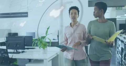 Two colleagues walking and discussing while holding folders in modern open-plan office