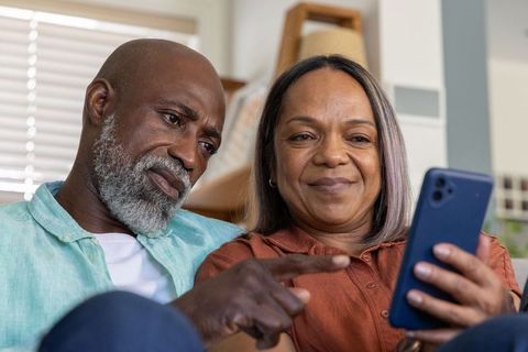 Senior couple using smartphone on couch at home sharing moments and browsing together