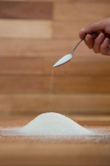 Woman hand pouring sugar from spoon on wooden table