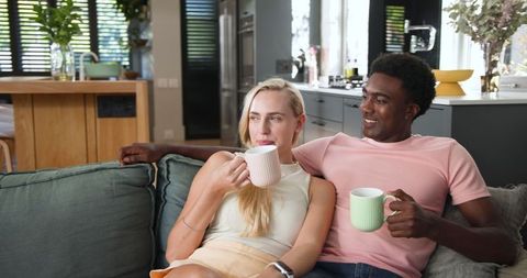 Diverse Couple Relaxing in Modern Cozy Living Room with Sipping Mugs