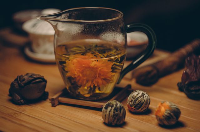 Blooming flower tea is steeped in a glass teapot placed on a wooden table. The fascinating visual of the bloom opening creates a serene ambience. Ideal for use in blog posts about tea culture, relaxation, or healthy living. Also suitable for depicting calming environments in advertisements or social media content promoting warm beverages.