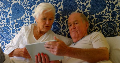 Senior Couple Engaged with Tablet Sitting on Bed