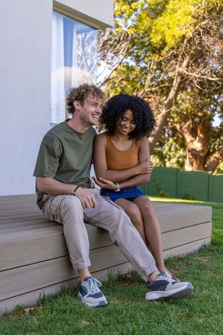 Interracial couple enjoying sunny backyard moment on raised deck in casual sneakers and denim skirt