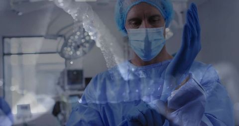 Surgeon donning sterile gloves in operating room before procedure with surgical lights