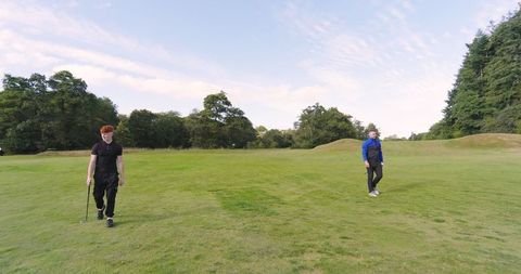 Father and Teenage Son Walking on Golf Fairway with Clubs
