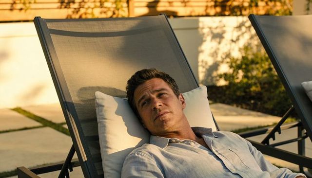 Reclining man gazing upward on sunlit backyard lounge chair with pillow and soft shadows