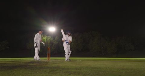 Night cricket under floodlights batsman preparing shot with wicketkeeper behind stumps
