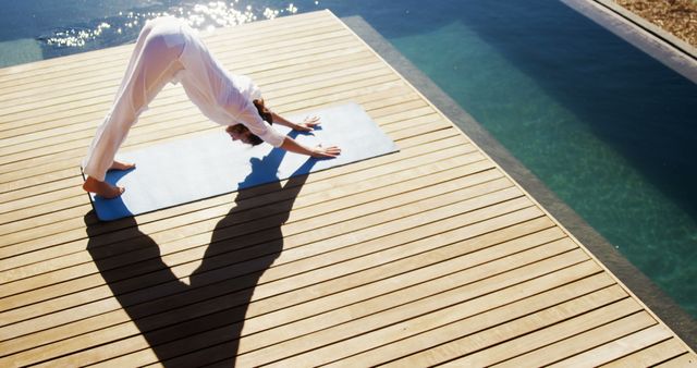 Woman practicing a yoga pose on wooden deck by the swimming pool on a sunny day. Ideal for relaxed lifestyle content, wellness blog articles, fitness inspiration, or advertisements related to yoga retreats and outdoor activities.