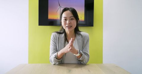 Asian businesswoman presenting sustainability pitch at meeting table with wind turbines