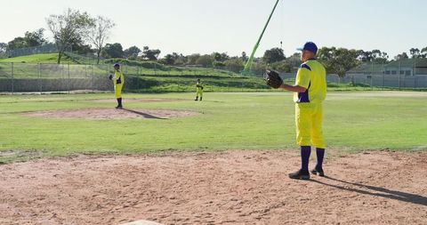 Three male baseball players standing on sunlit infield wearing bright yellow uniforms
