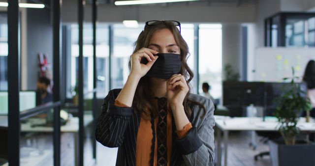 Businesswoman Removing Face Mask in Modern Office Environment - Download Free Stock Images Pikwizard.com