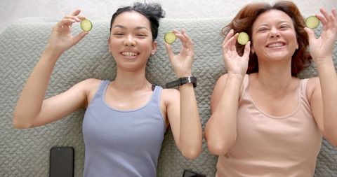 Two female friends enjoying spa day with cucumber slices and smiling