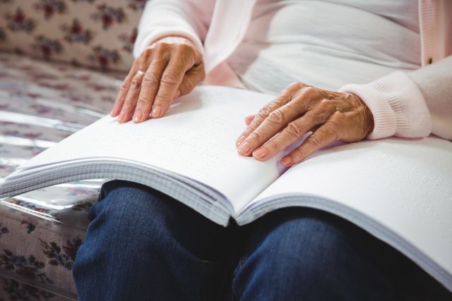Senior woman reading a braille book in a retirement home. This image highlights accessibility and independence for the visually impaired elderly. Ideal for use in articles about aging, disability support, retirement living, and inclusivity.