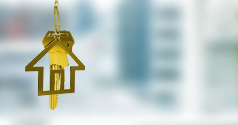 A golden key with a house symbol keychain is suspended in front of a blurred interior background, providing ample copy space. This visual is ideal for illustrating concepts of home ownership, real estate transactions, and new property acquisition, making it excellent for real estate advertising, investment blogs, and interior decor promotions.