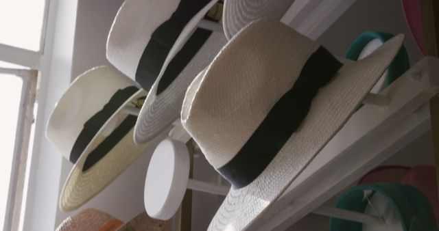 This image features stylish wide-brimmed white sun hats with black ribbon bands displayed on a shelf, with natural window light illuminating the scene. Perfect for content related to summer fashion, accessories shopping, stylish headwear, seasonal trends, and retail displays.