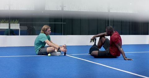 Diverse Friends Relaxing on Blue Padel Court After Game