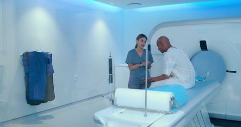 African american mri technologist consulting male patient on scanner table in imaging suite