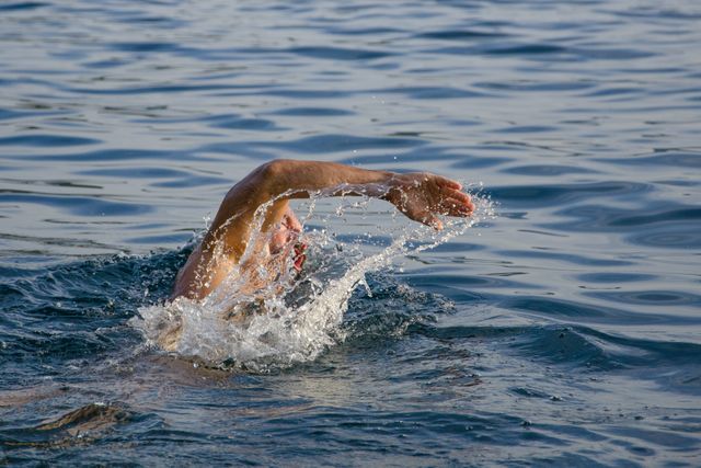 Man performing freestyle stroke in open water. Splashing water shows fast motion. Suitable for themes related to fitness, swimming techniques, outdoor sports, and health benefits of swimming.