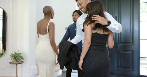 African american friends greeting couple hugging in stylish modern entryway