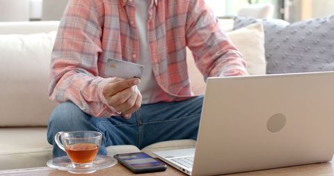 Man Holding Credit Card Shopping Online Using Laptop at Home