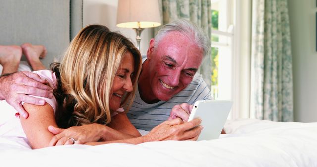 Smiling couple lying on bed and using digital tablet in bed room